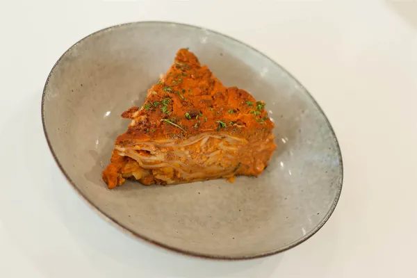 A wedge of house lasagna in a stoneware bowl